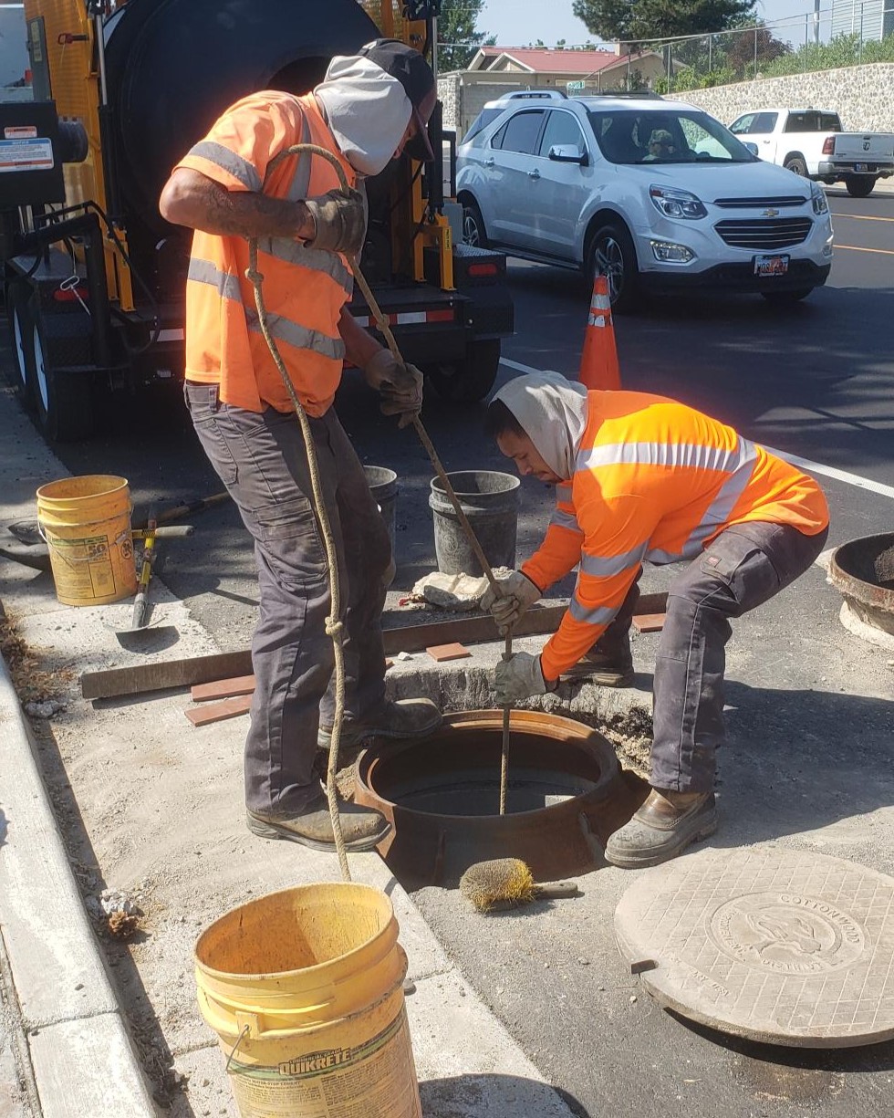 Two workers are shown installing a sewer manhole ring.